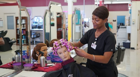 A Cosmetology student works on a mannequin in the Advanced Student Clinic
